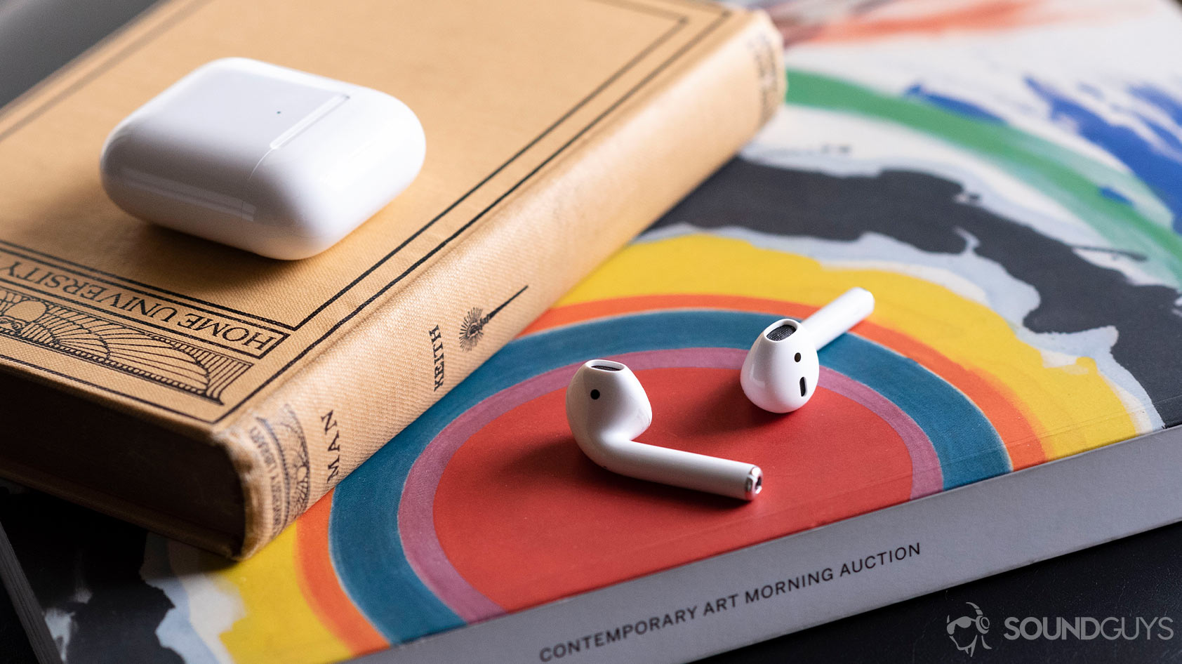 Apple new AirPods 2_earbuds case separate The Apple AirPods 2019 on an arts magazine with the case above it, shut.