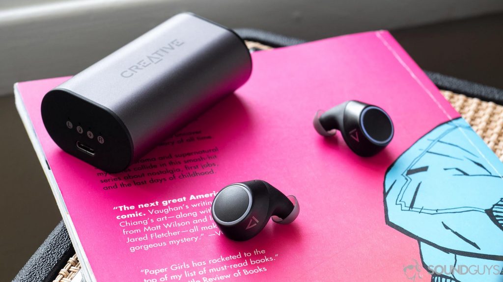 Creative Outlier Air: The earbuds outside of the case resting on a pink and blue comic book with the charging case in the background.