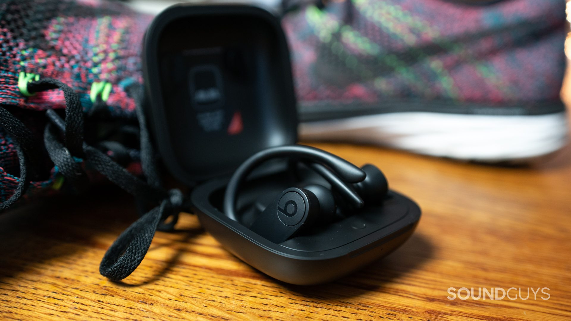 A photo of the Powerbeats Pro on a wooden floor next to running sneakers.