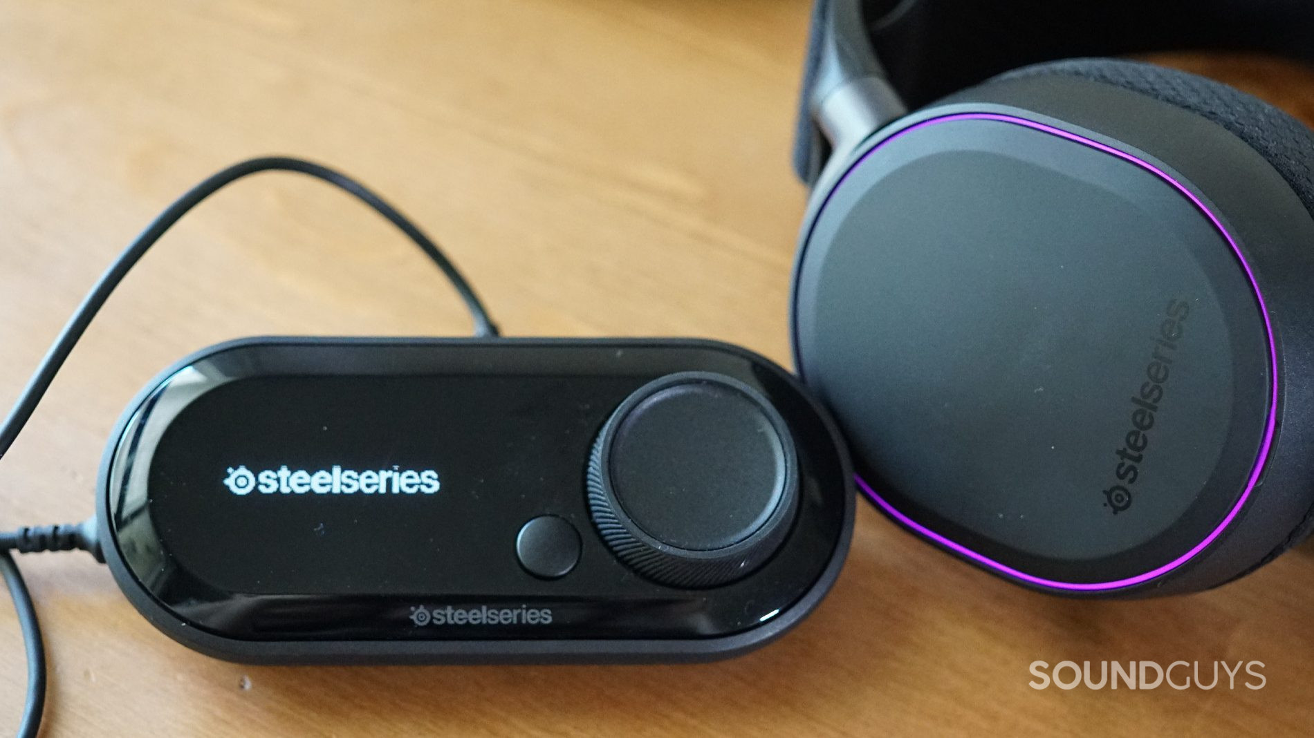 The SteelSeries Arctis Pro + GameDAC sits on a wooden table plugged in and turned on.