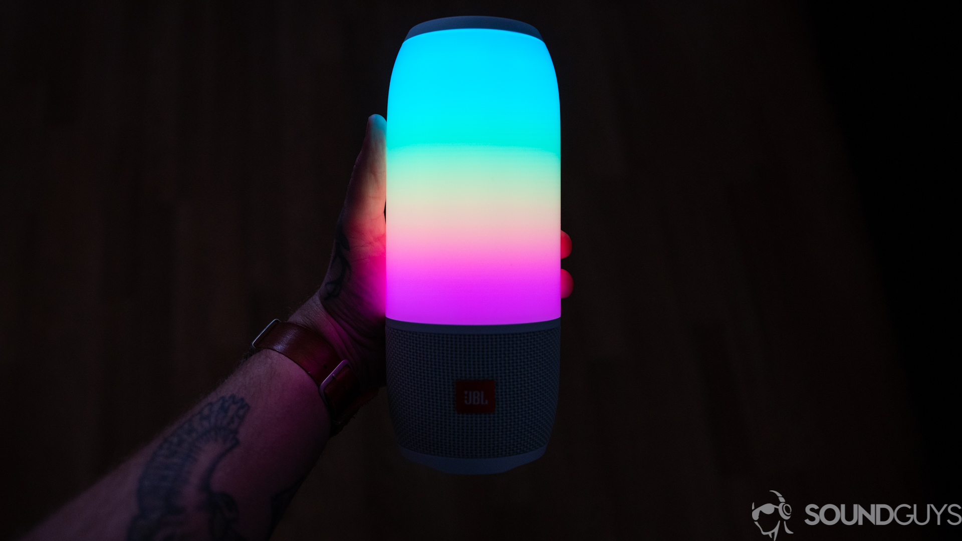 Shot of the colorful lights of the JBL Pulse 3 held in hand in a dark room.