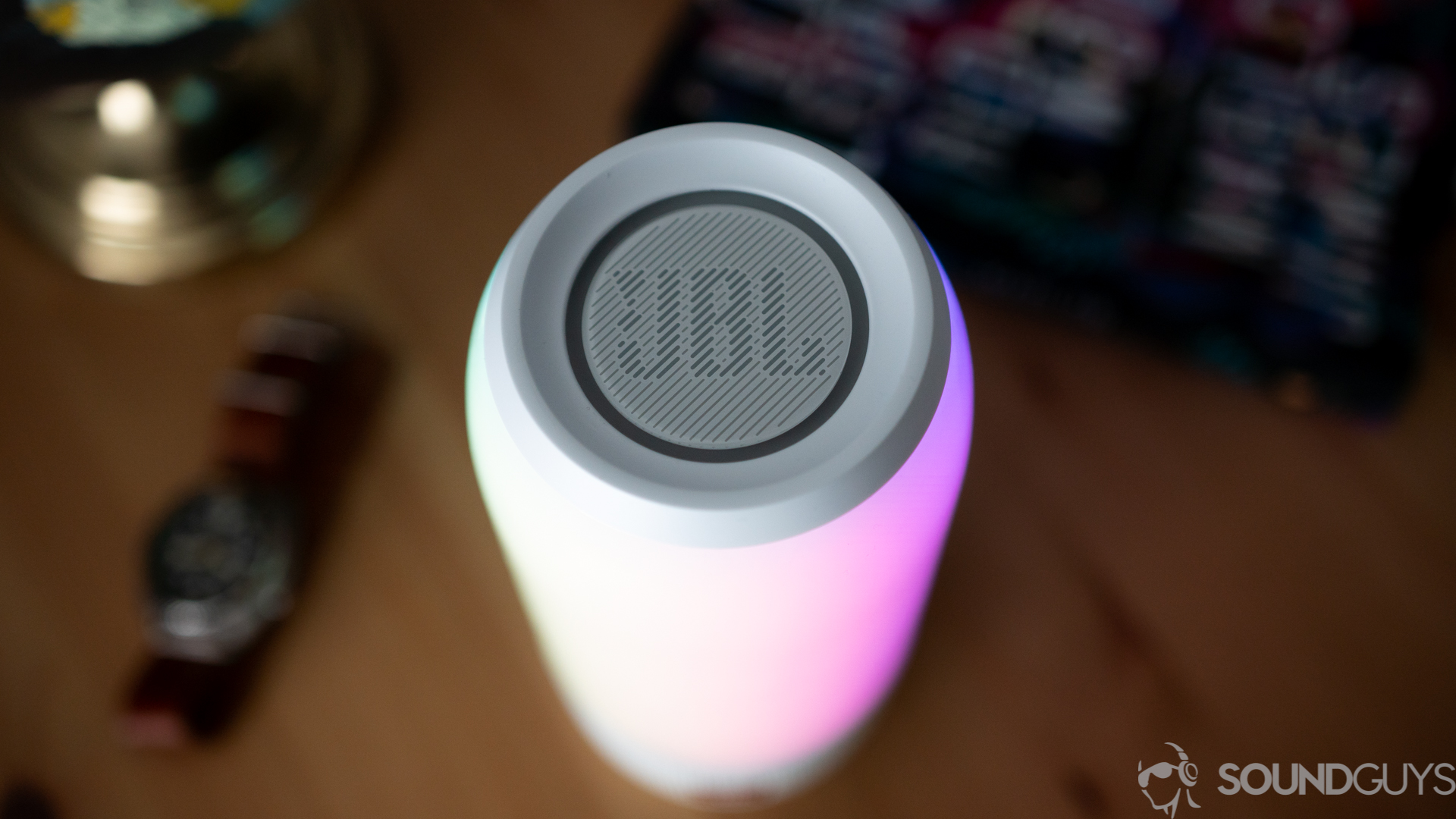 Shot of the JBL logo on the top of the Pulse 3 speaker with a watch and globe in the background. 