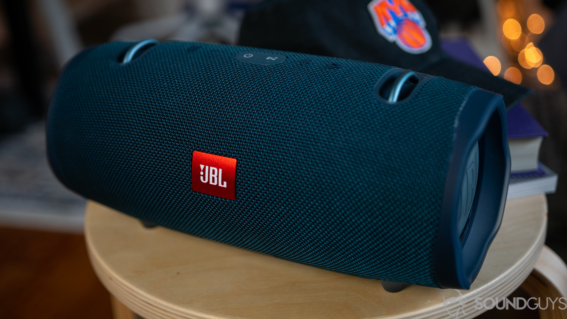 Close up of the blue JBL Xtreme 2 speaker on a wooden stool with a hat in the background.