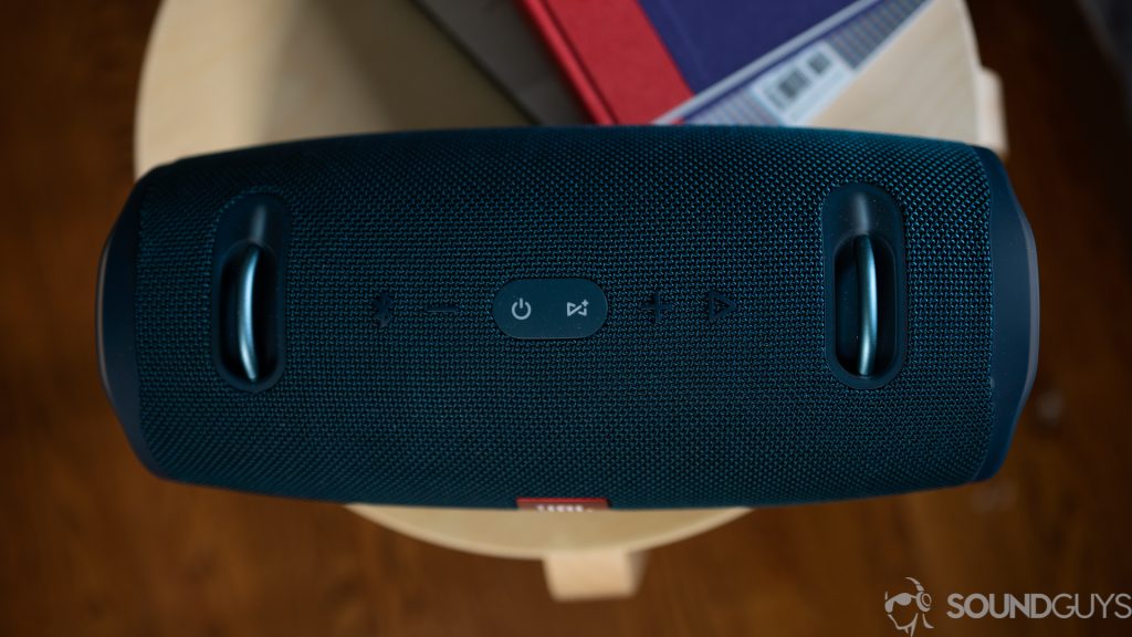 Pictured are the playback buttons on top of the JBL Xtreme 2 speaker on a wooden stool with books. 