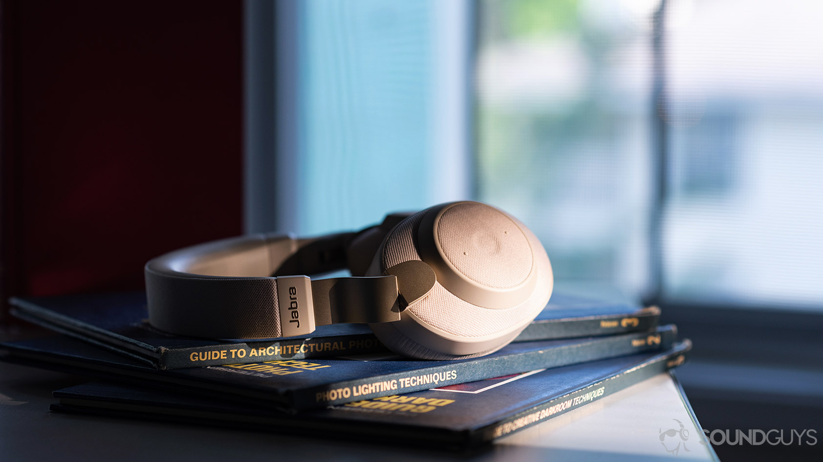 The Jabra Elite 85h headphones in front of a window on a stack of books.