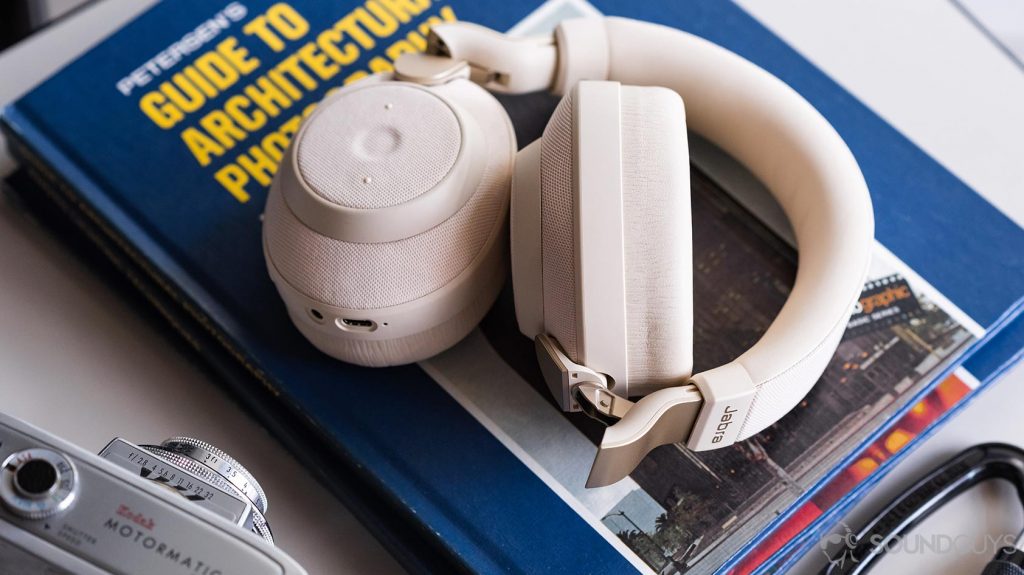 The Jabra Elite 85h headphones partly folded on a stack of blue, thin books with a vintage camera in the bottom left corner.