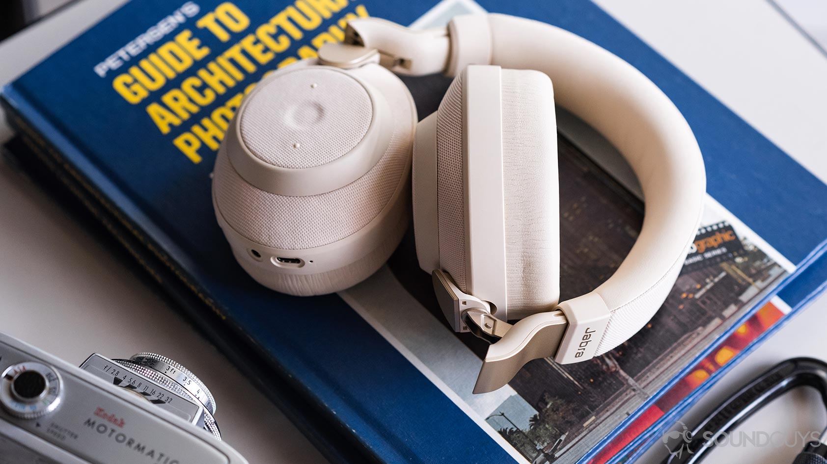 A photo of the Jabra Elite 85h headphones partly folded on a stack of blue, thin books with a vintage camera in the bottom left corner.