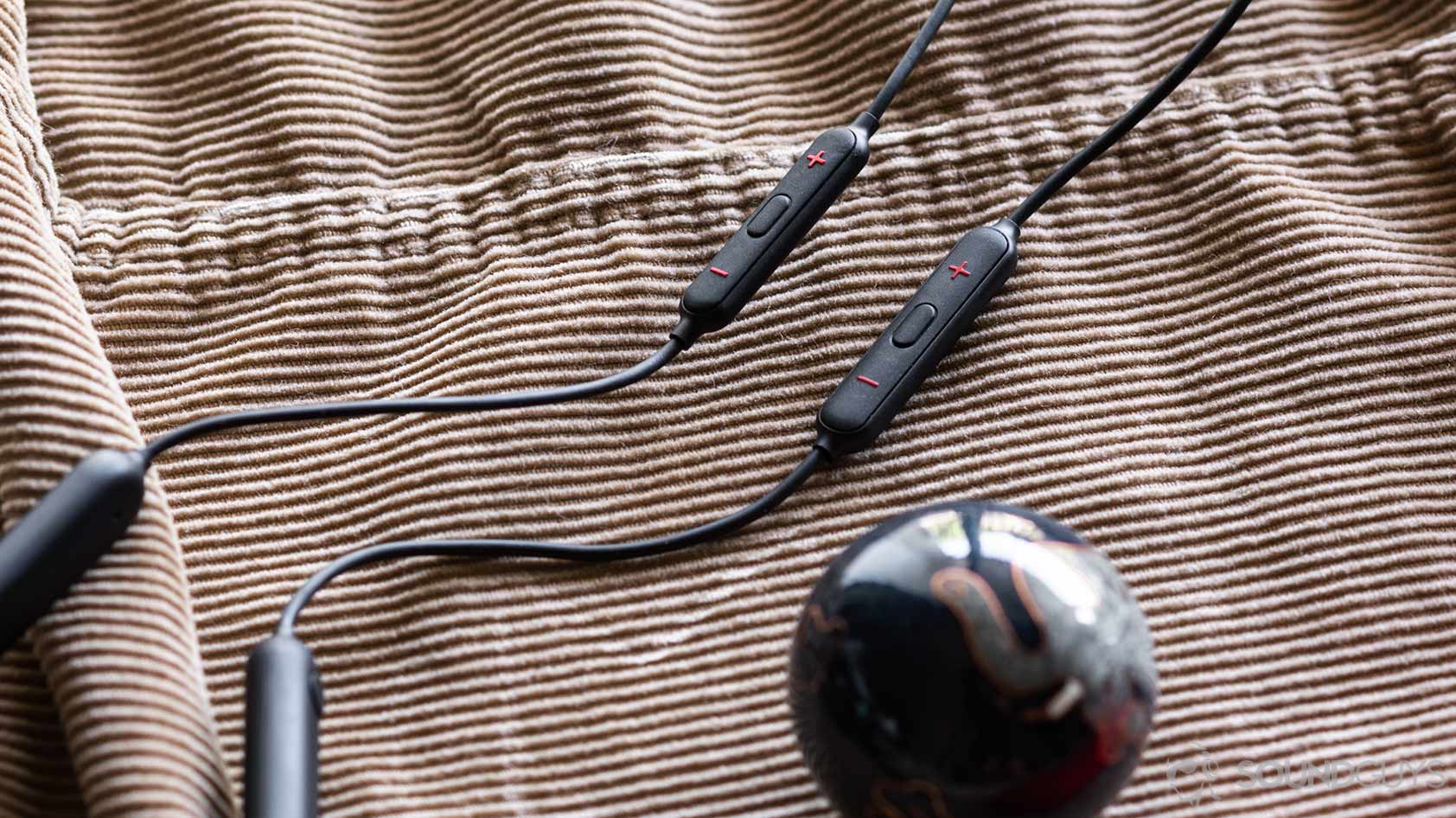 A picture of the OnePlus Bullets Wireless 2 next to the old Bullets Wireless remote and new one on corduroy jacket.