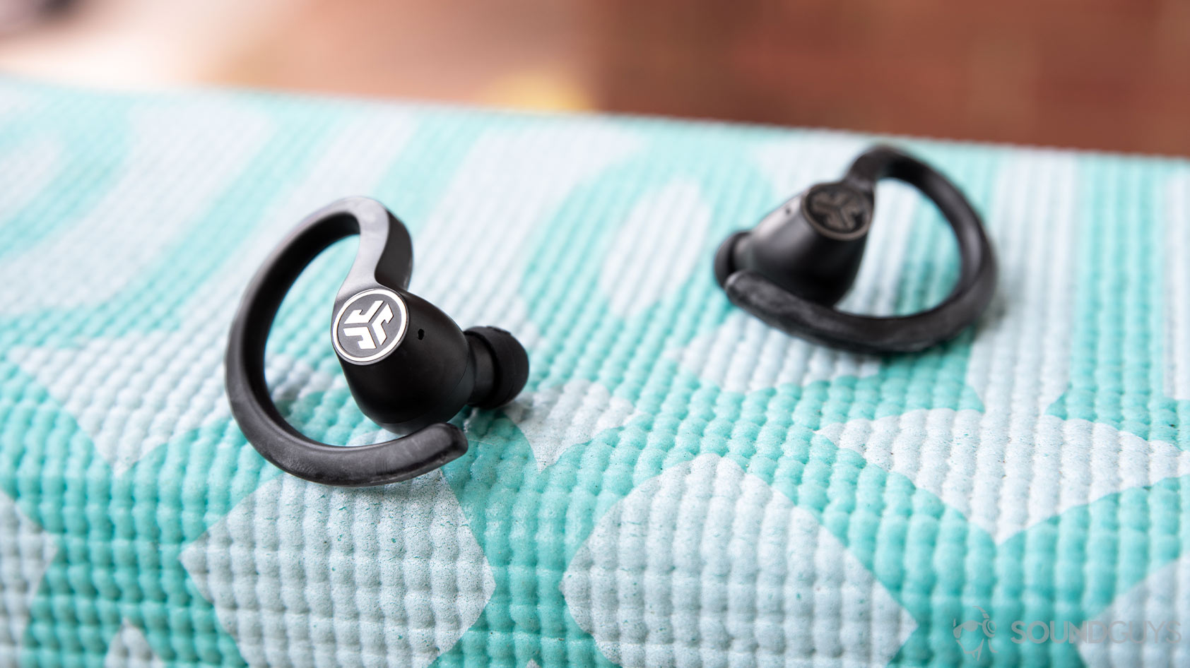 A picture of the JLab JBuds Air Sport resting on a teal yoga mat.