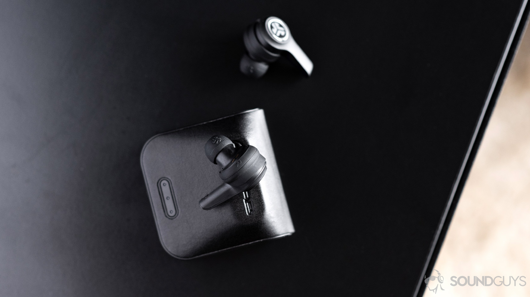 Aerial image of the JLab JBuds Air Executive. One earbud is atop the closed case and another is off to the side.
