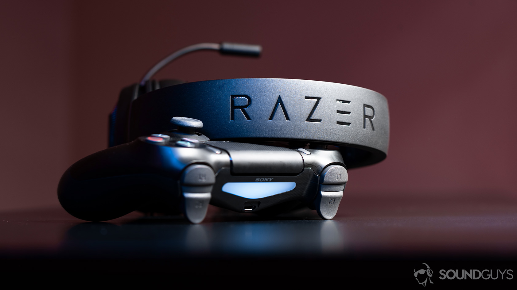The Razer Kraken cheap gaming headset leaning against a PS4 controller with the headband facing the lens to show the Razer logo.