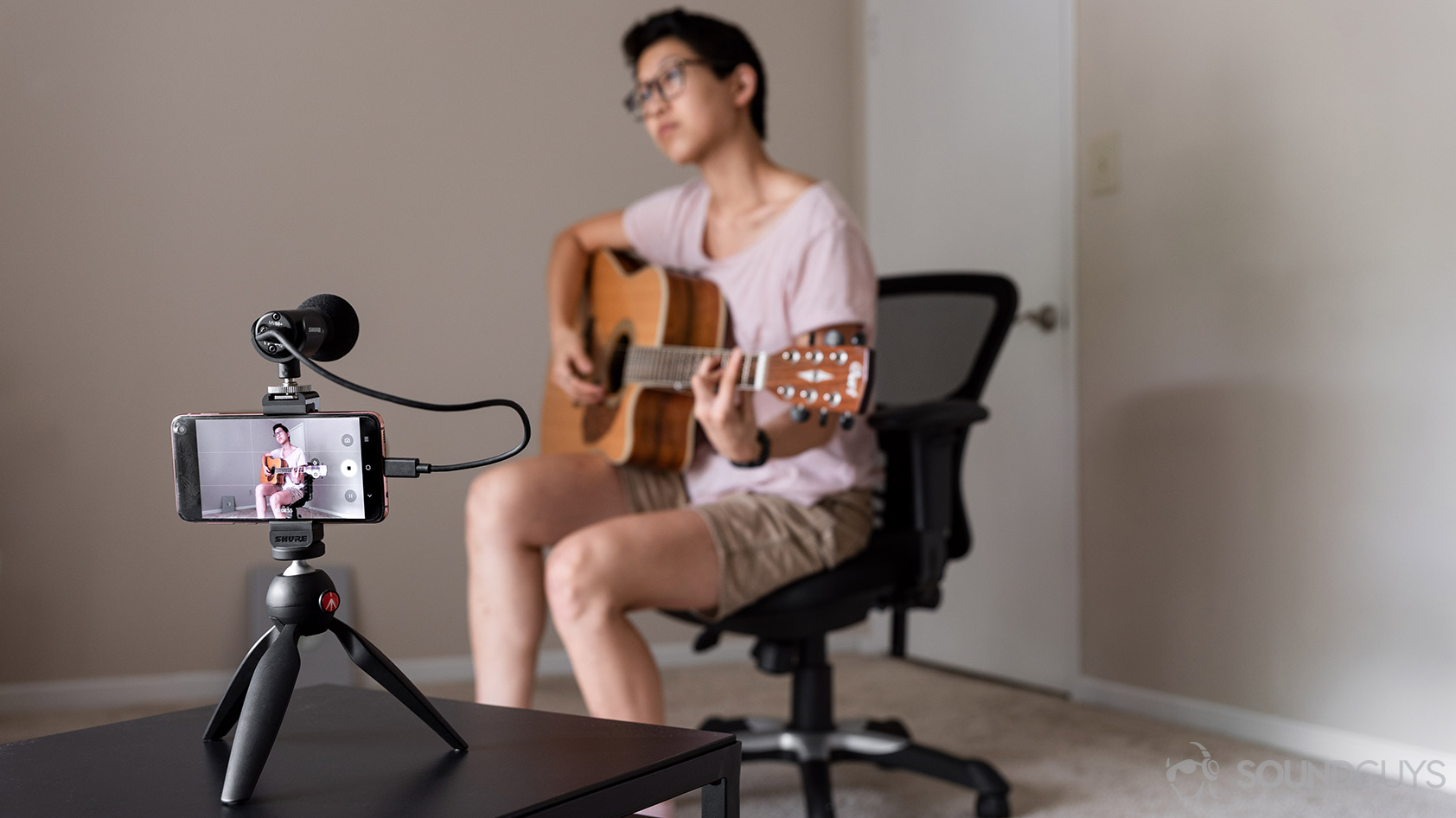 Woman playing guitar in front of the Shure MV88+ Video Kit attached to a Samsung Galaxy S10e smartphone.