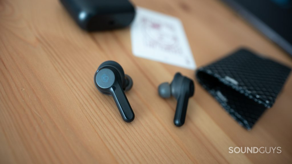 The Skullcandy Indy true wireless earbuds on a wood desk next to a playing card and black wallet.