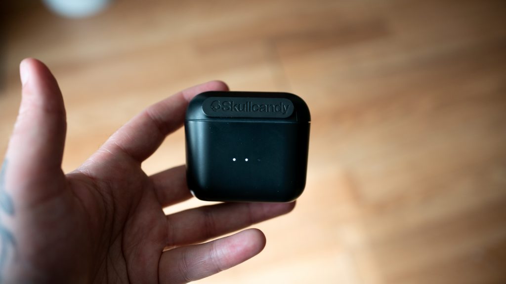 Man holding the Skullcandy Indy charging case in hand with the LED lights lit up.