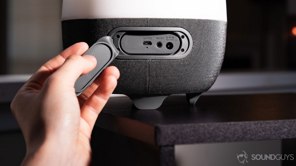 A hand opening the rubberized door to reveal three inputs: microUSB, aux, and power.