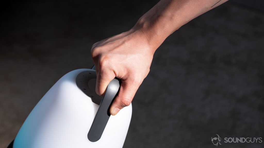 A hand carrying the speaker by the plastic handle.