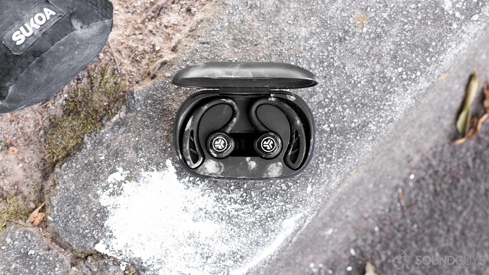 A picture of the JLab JBuds Air Sport, the more premium JLab JBuds Air Sport, in the charging case with rock climbing chalk on the curb surface.