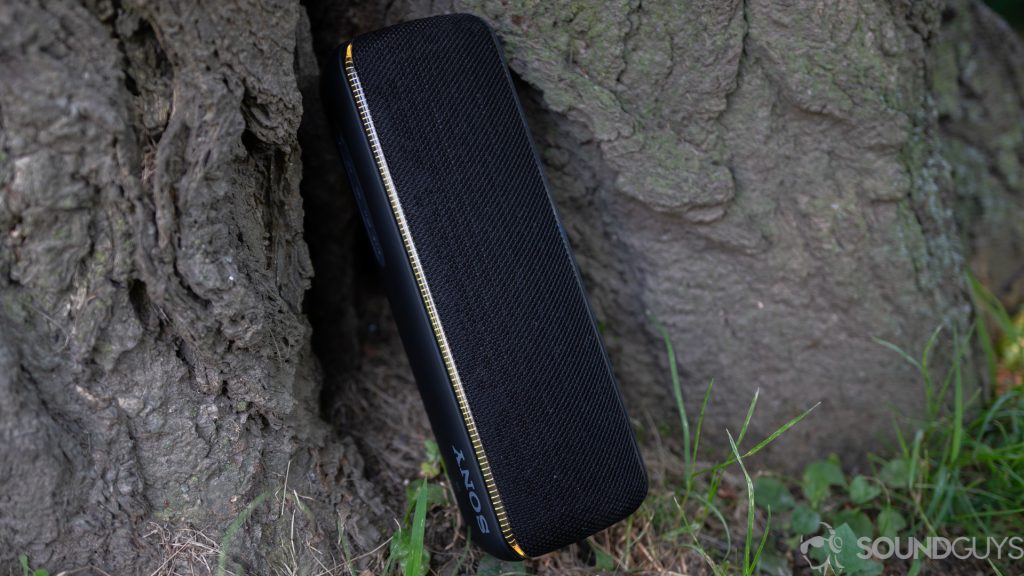 The Sony SRS-XB32 Bluetooth speaker leaning against a tree with its colorful lights turned on. 