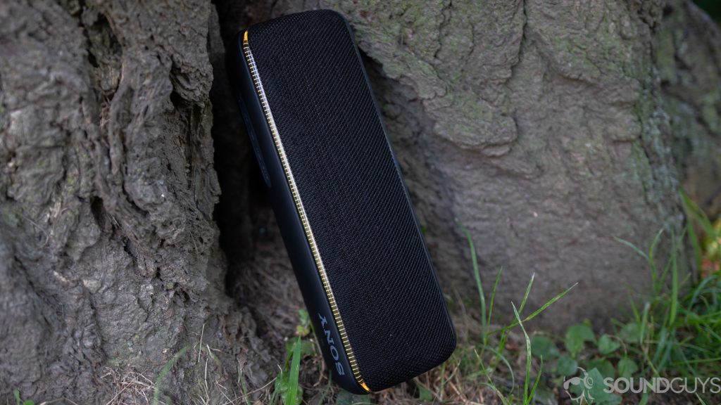 The Sony SRS-XB32 Bluetooth speaker leaning against a tree with its colorful lights turned on.