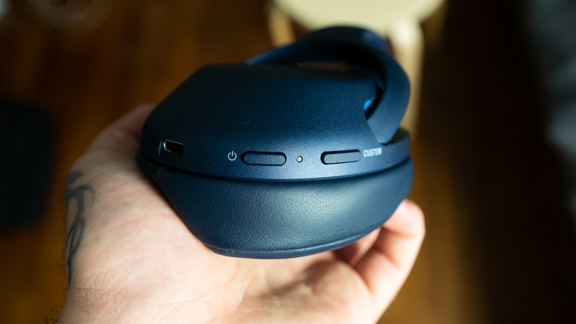 Picture of the Sony WH-XB900N headphones in hand with a focus on the power button. 