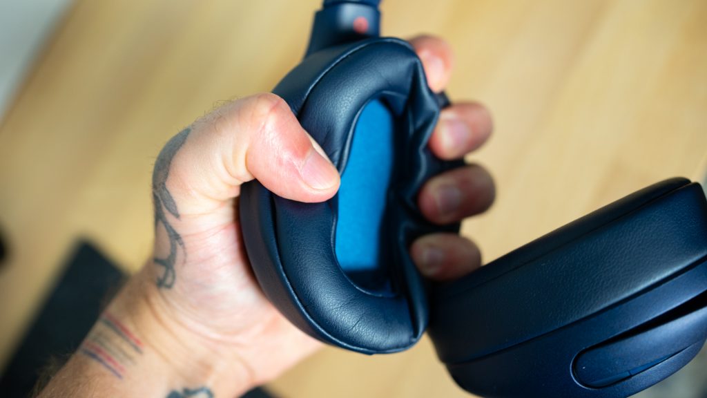 A photo of a man's left hand crushing the padding on the WH-XB900N headphones.