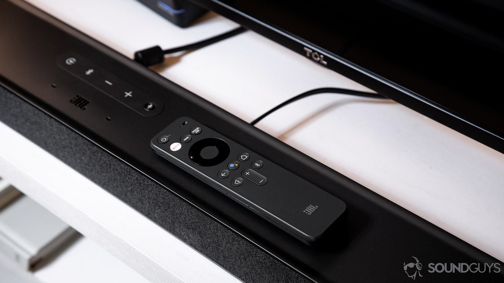 JBL_Link Bar-6_smart speaker soundbar Google Assistant remote Netflix TLC TV The JBL Link Bar remote lying atop the smart soundbar in front of a TLC TV.