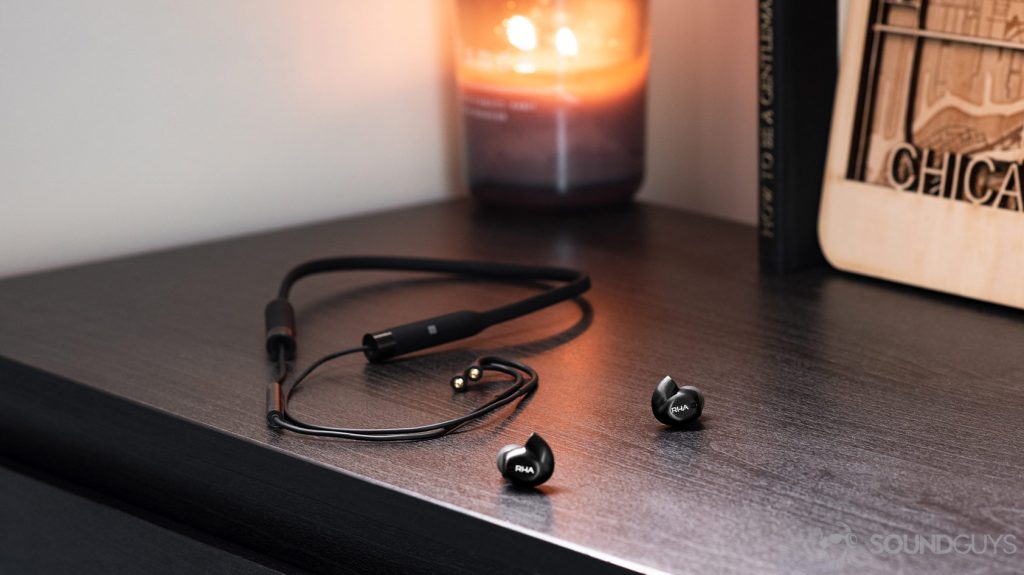 A photo of the RHA T20 Wireless earbuds detached from the wireless neckband on a wood surface with a candle in the background.