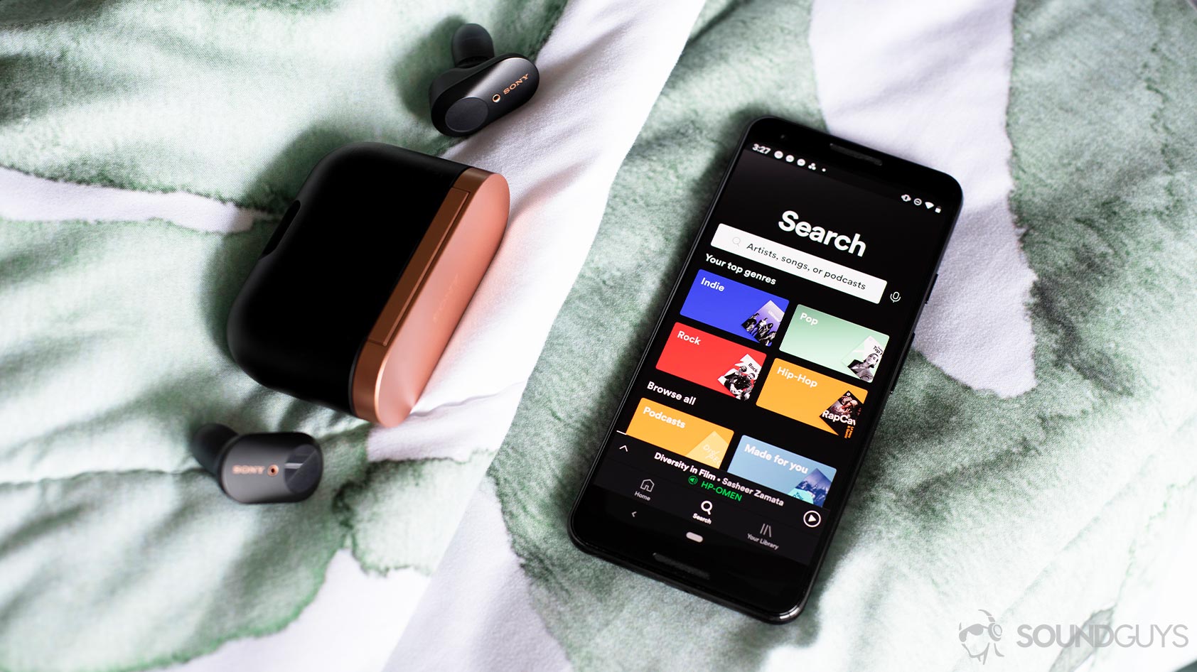 A Google Pixel 3 on a comforter next to the Sony WF-1000XM3 true wireless earbuds and charging case.