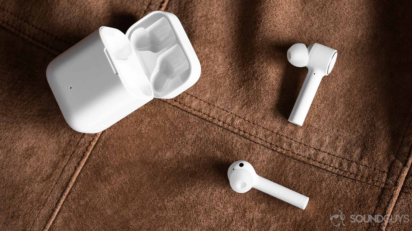 Aerial image of the Xiaomi Air TWS earbuds outside of the charging case, which is laying open on a suede surface.