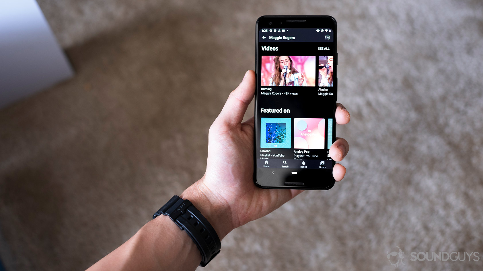 A hand holding a Google Pixel 3 with the YouTube Music Premium app open to the search function.