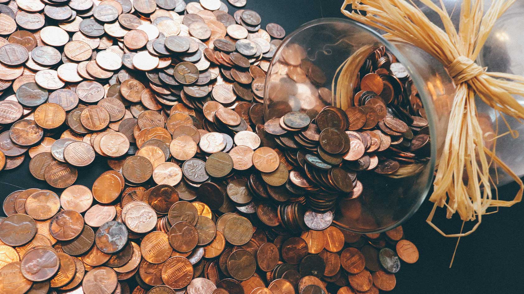 money coins pennies spilling jar Pennies spilling onto a table from a glass jar.