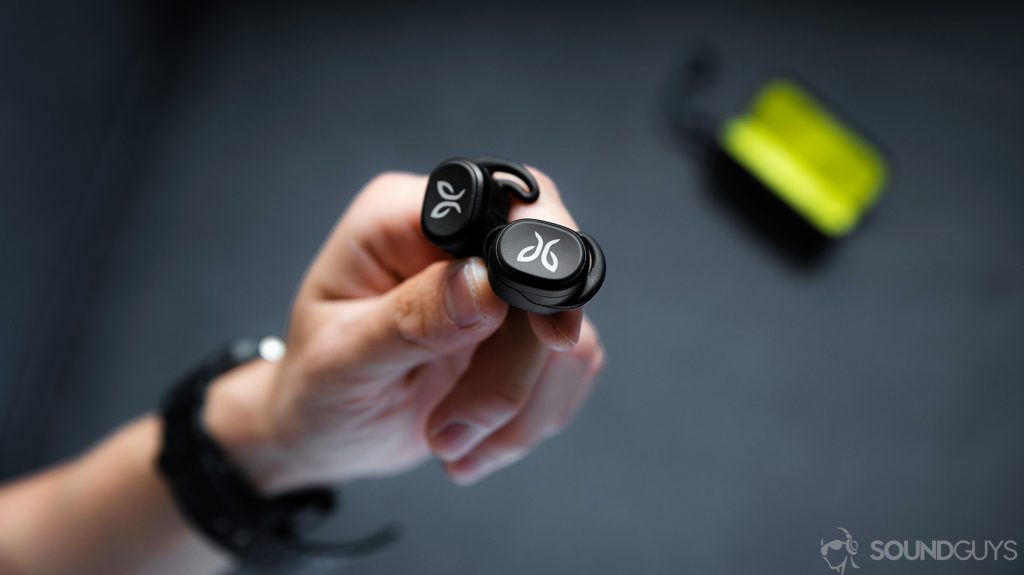 The Jaybird Vista earbuds being held in a hand with the open charging case in the background.
