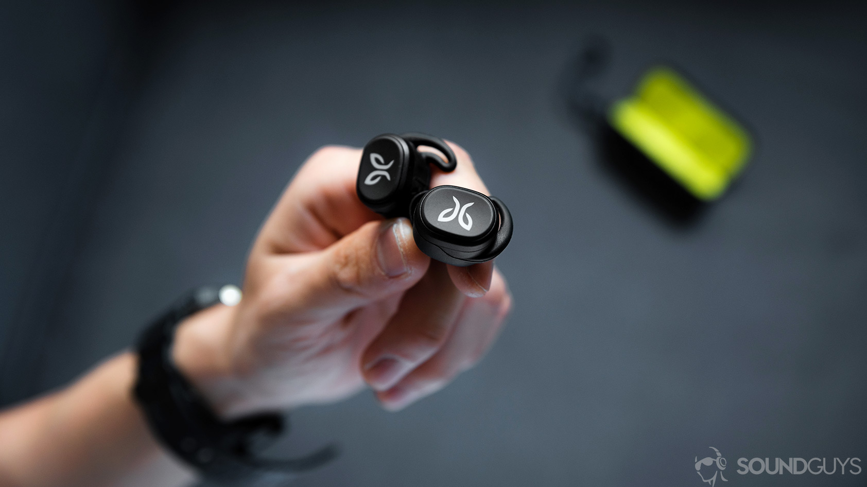 Jaybird Vista-5_earbuds hands on open charging case The Jaybird Vista earbuds being held in a hand with the open charging case in the background.