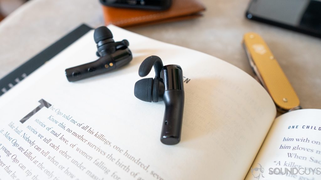 A photo of the Treblab X5 true wireless earbuds sitting on a book, near a wallet and pocketknife.
