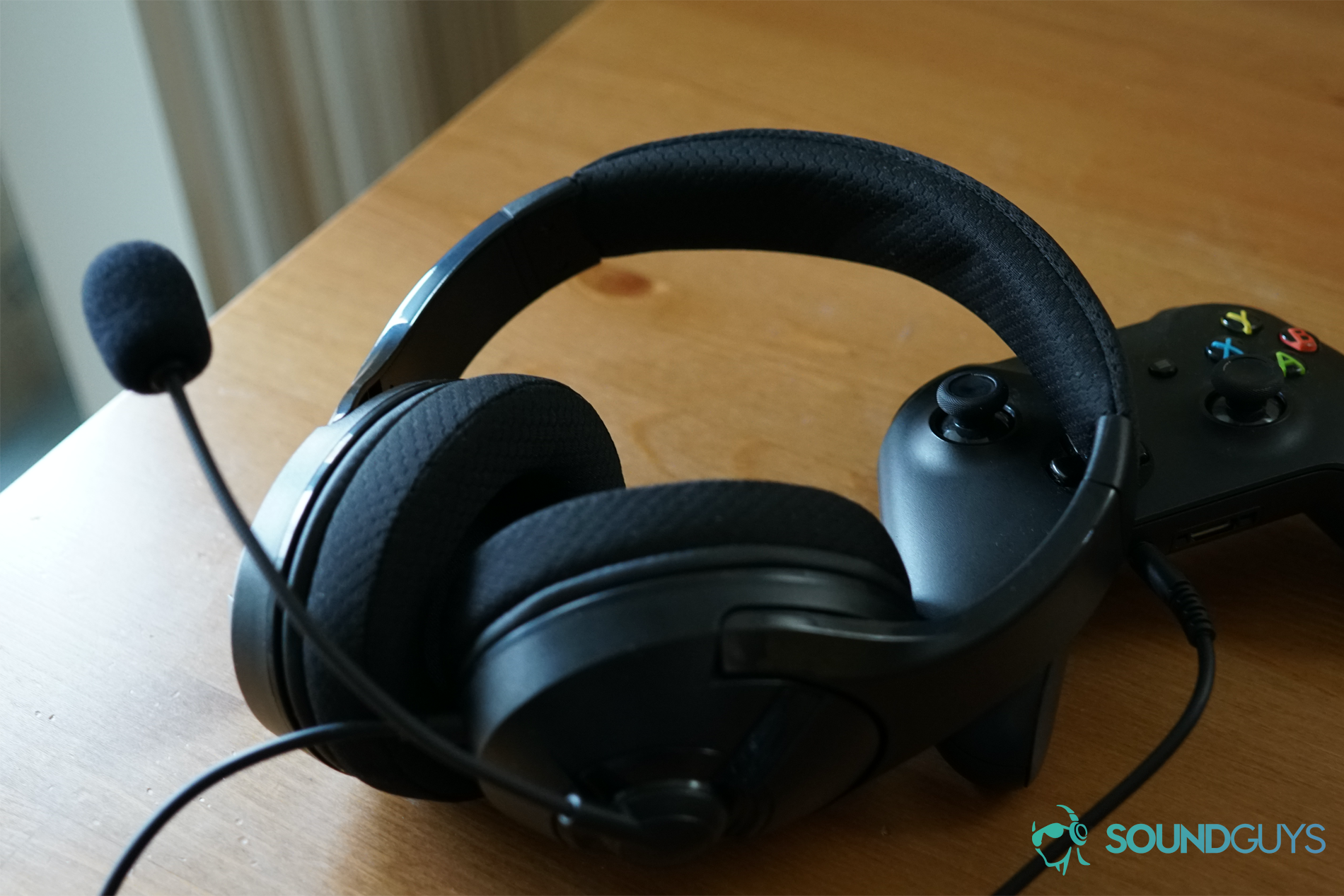 The AmazonBasics Gaming headset leaning on and plugged into an Xbox One controller on a wooden table.