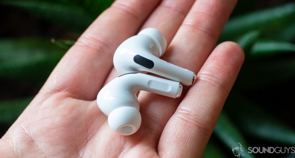 The Apple AirPods Pro in a man's left hand against a green background.