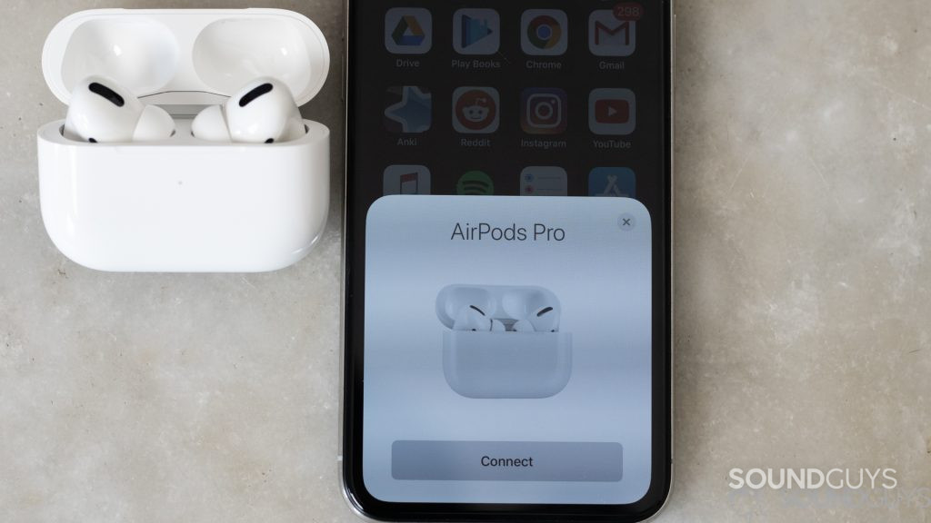 The AirPods Pro in the open case rest next to an iPhone that displays a pairing request pop-up notification.