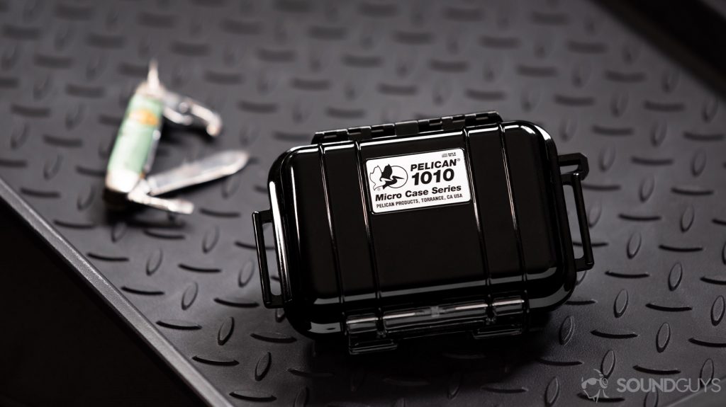 A photo of the Massdrop x Noble Kaiser 10 Universal's Pelican hardshell carrying case on a tough, textured surface with a multi-purpose knife in the background.