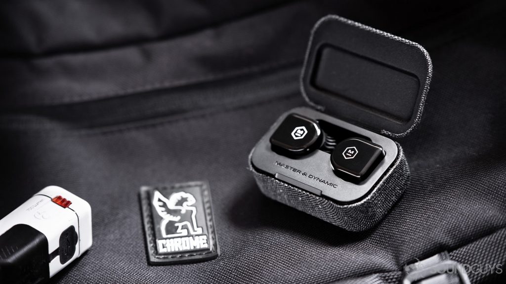 An image of the Master & Dynamic MW07 Go true wireless earbuds in the open charging case atop a Chrome Industries messenger bag.