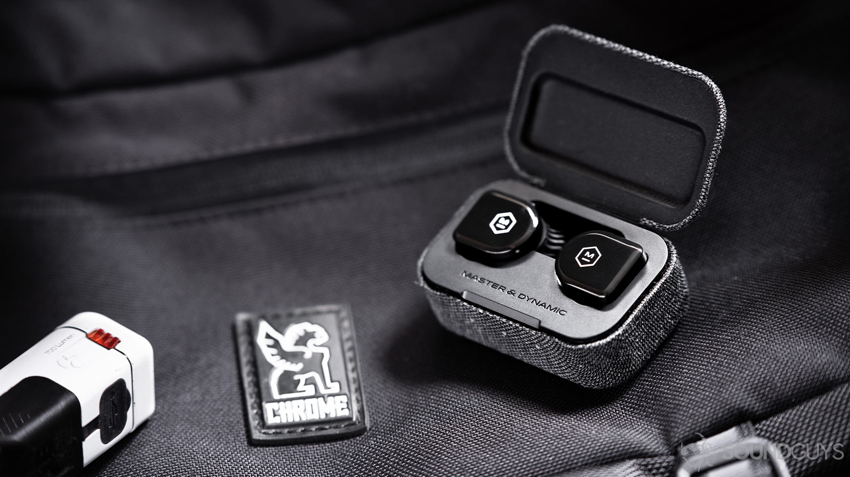 The Master &amp; Dynamic MW07 Go true wireless earbuds in the open charging case atop a Chrome Industries messenger bag.