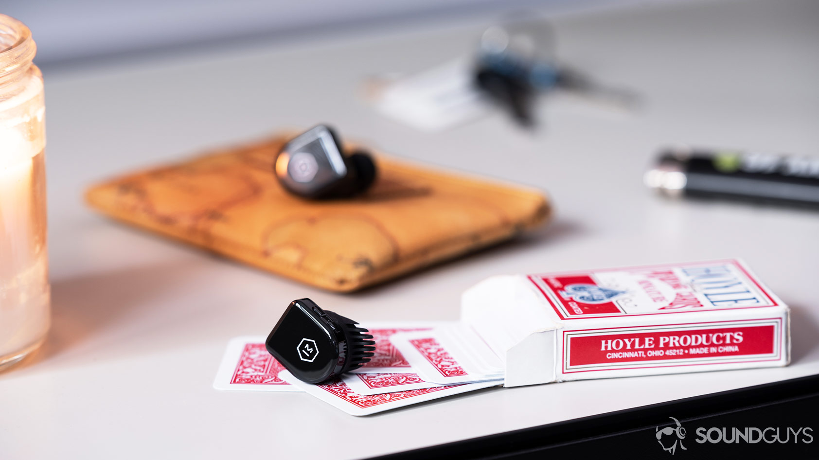 Master & Dynamic MW07 Go-true wireless earbuds table cards logo An image of the Master & Dynamic MW07 Go true wireless earbuds on red, miniature playing cards with a candle, keys, lighter, and coin pouch in the background.