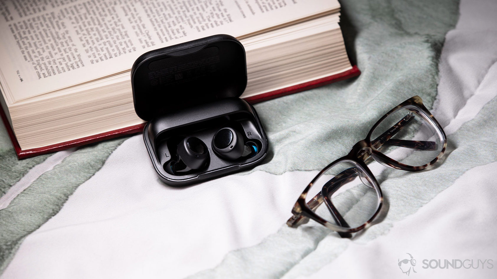 A picture of the Amazon Echo Buds in the case next to glasses and a book.