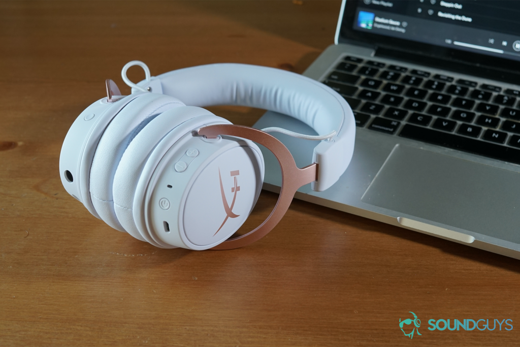 The HyperX Cloud Mix sits on a wooden table, resting on a Macbook Pro running Spotify.