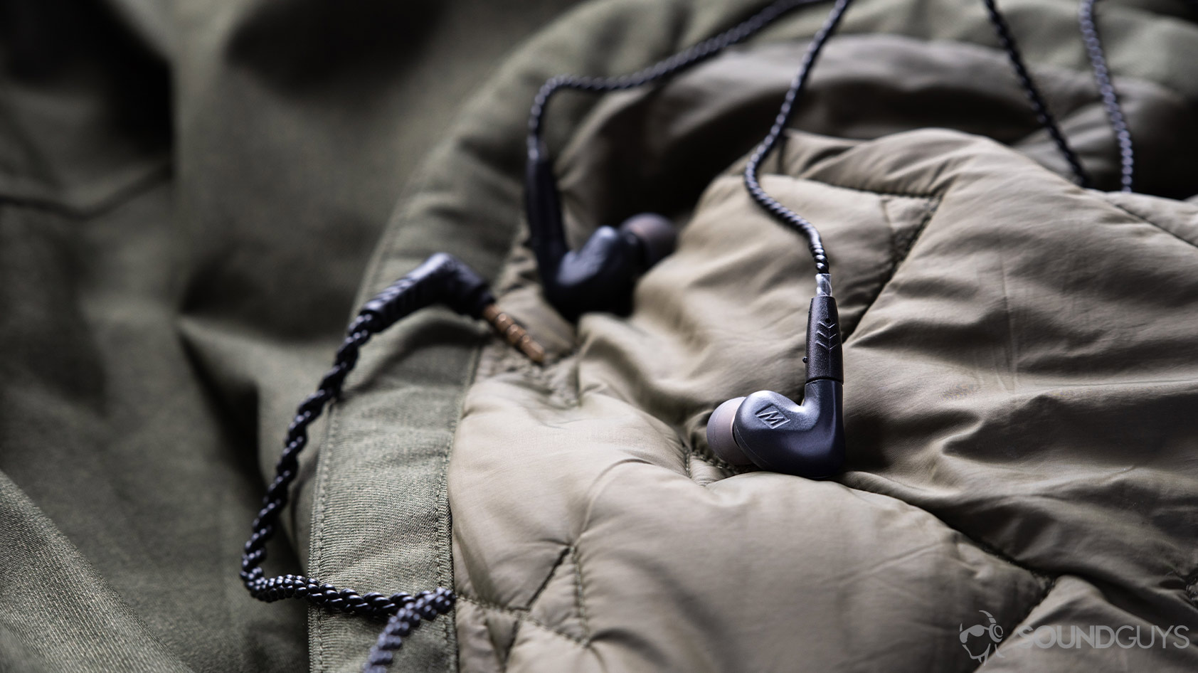 A photo of the Massdrop x MEE audio Pinnacle PX earbuds on a quilted green surface.