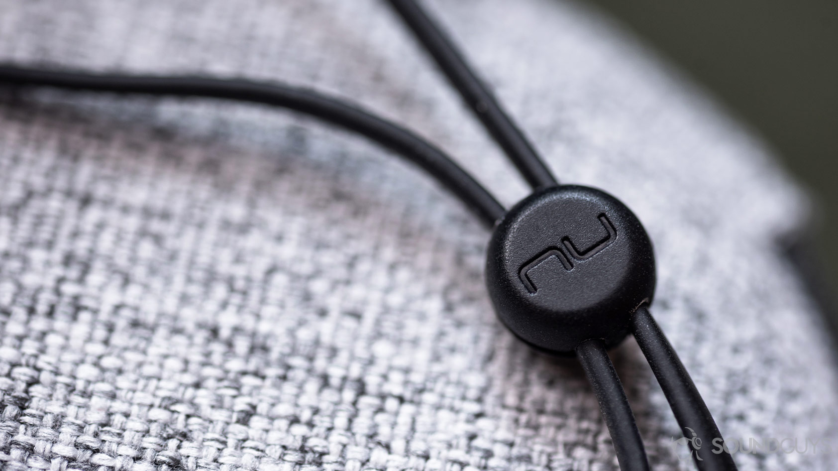 A macro photo of the Massdrop x NuForce Stride wireless earbuds (blue) of the NuForce-branded cable cinch mechanism.