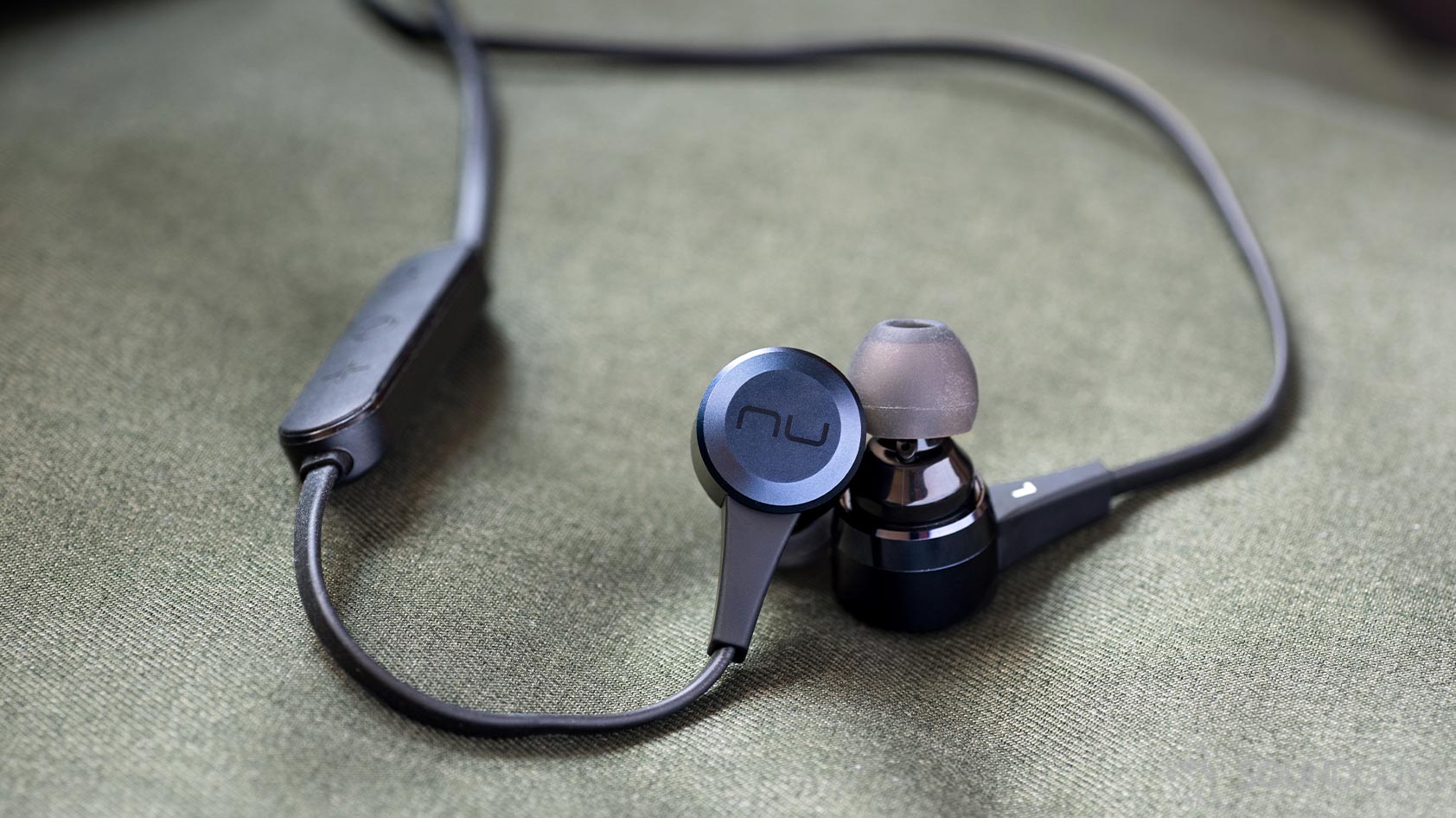 A photo of the Massdrop x NuForce Stride wireless earbuds (blue) and the NuForce logo on the earbuds.