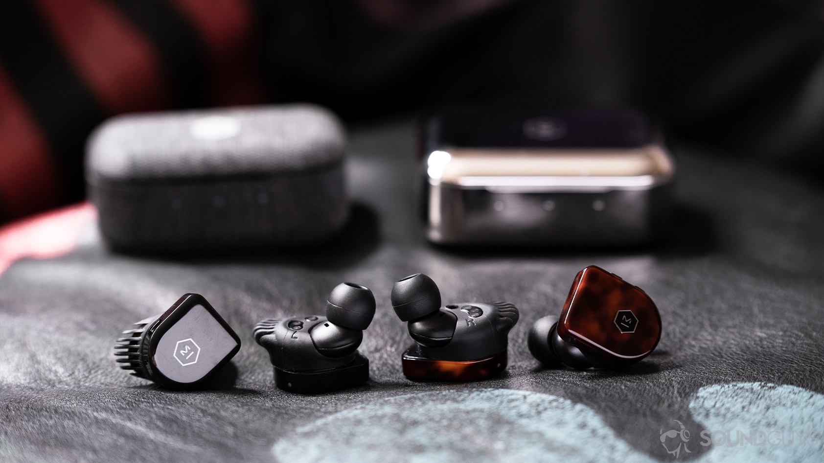 A picture of the Master &amp; Dynamic MW07 Plus and MW07 Go noise canceling true wireless earbuds and charging cases next to each other on a leather surface.