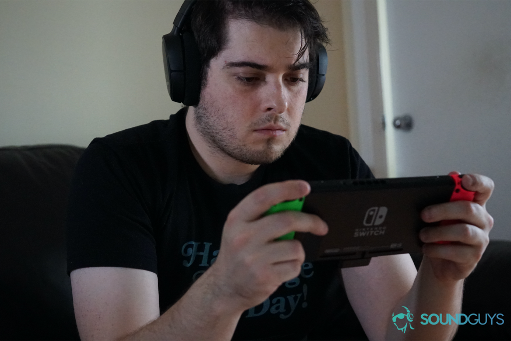 A man sits on a couch playing a Nintendo Switch with the SteelSeries Arctis 1 Wireless gaming headset.