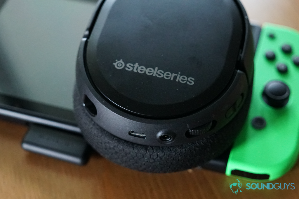 The SteelSeries Arctis 1 Wireless rests on a Nintendo Switch with the USB-C dongle plugged into it on a wooden table.