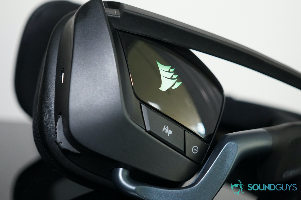 The Corsair Void RGB Elite Wireless gaming headset lies on its side, with its in ear controls visible and its RGB lights on.